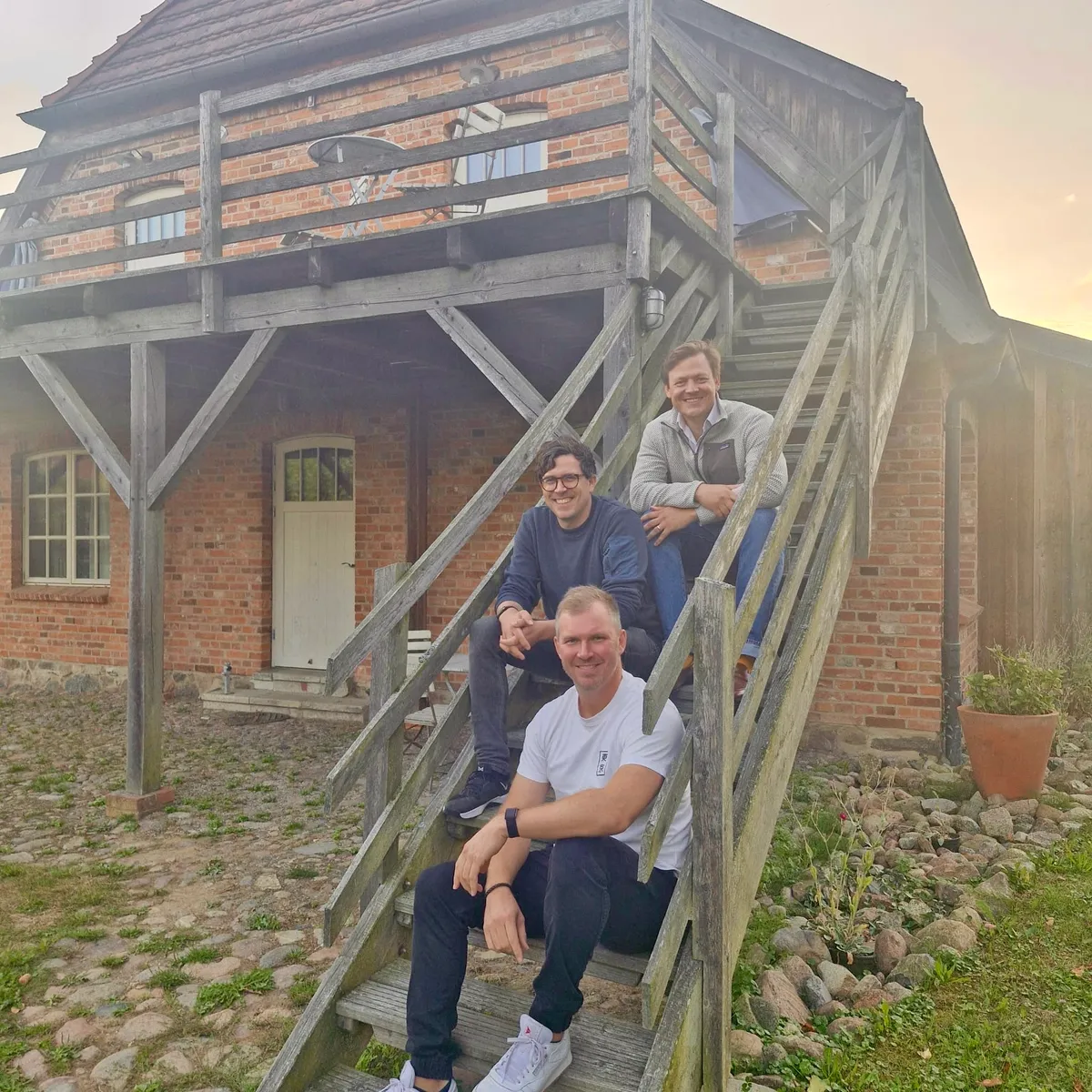 Die drei Jurafuchs-Gründer sitzen auf einer Holztreppe vor einem Backsteinhaus